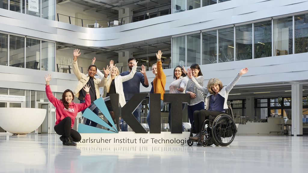 Diverse group posing cheerfully by KIT sign at Karlsruhe Institute of Technology.
